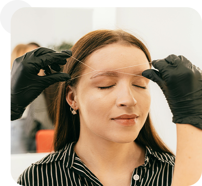 A woman getting her eyebrows threaded by two hands.