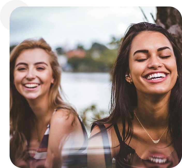 Two women smiling and laughing together outside.